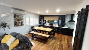 A compact kitchen with a dining area, wooden flooring, and black cabinetry. - Landwin Gardens 1 - walk to the beach (SOUTH WEST ROCKS)