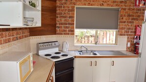 A compact kitchen with a stove, sink, and window overlooking a brick wall.