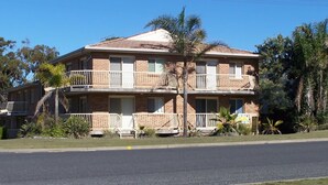 A two-story building with balconies, surrounded by greenery and a clear sky.