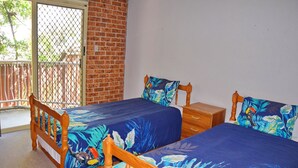 A bedroom with two wooden beds, a nightstand, and a window with a view of a fence and trees.