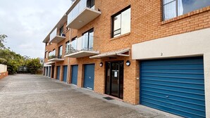 Une rangée d’immeubles en briques avec des portes de garage bleues, numérotées 2, et une petite enseigne sur la porte.