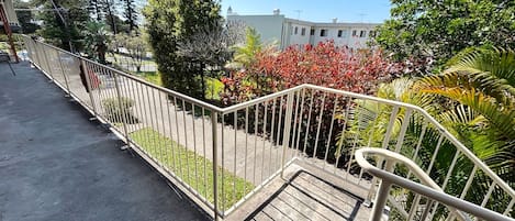 A balcony with a metal railing, a concrete floor, and a view of a building and trees.