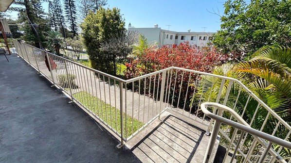 A balcony with a metal railing, a concrete floor, and a view of a building and trees.