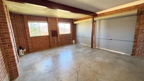 A spacious garage with brick walls, two large garage doors, and a concrete floor. - Horizons - South West Rocks (SOUTH WEST ROCKS)