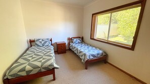 A bedroom with two single beds, a nightstand, and a window with a view of a fence.