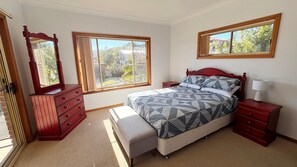 A bedroom with a bed, a dresser, a nightstand, a lamp, and two windows.