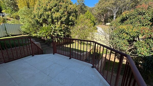 A patio area with a tiled floor, surrounded by a metal railing, and overlooking a garden with various trees and shrubs.