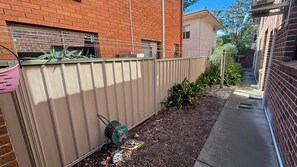 A residential area with a brick building, a metal fence, and a garden with mulch and plants.