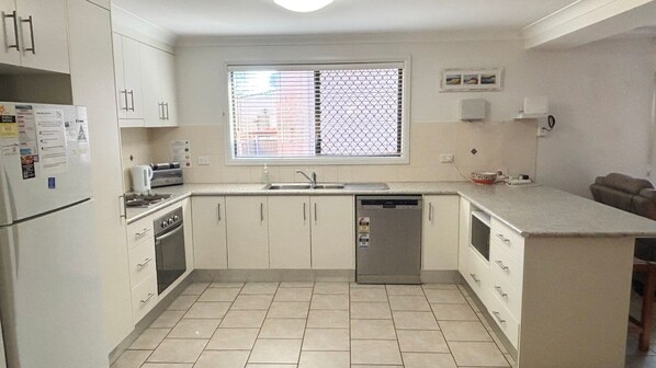 A compact kitchen with white cabinets, a stainless steel sink, and a tiled floor.