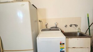 A compact kitchen with a white refrigerator, a washing machine, and a sink with a hose. - Parkside # 1 - South West Rocks - Bring your own linen (South West Rocks)
