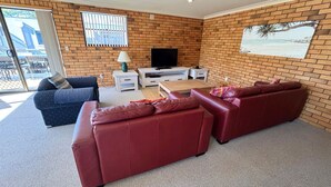 A living room with a brick wall, a TV, a sofa, a coffee table, and a window with blinds.