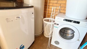 A laundry room with a front-loading washer and dryer, a white basket, and a brick wall.