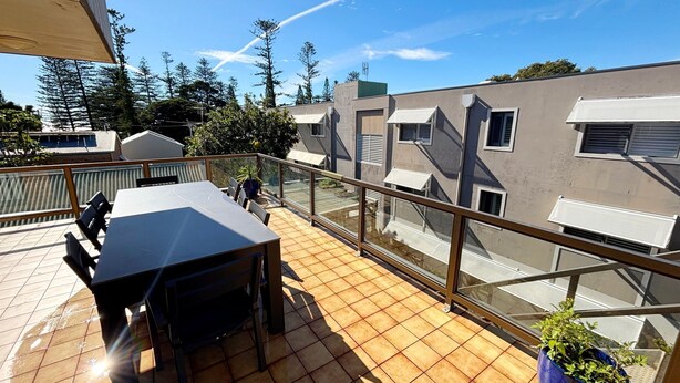 A balcony with a table and chairs, a view of neighboring buildings, and a clear sky.