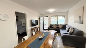 A compact living space with a dining area, a sofa, a television, and a clock on the wall. - Dunbar Court Unit 3 - South West Rocks (SOUTH WEST ROCKS)