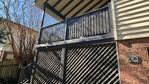 A two-story building with a balcony, a metal gate, and a brick wall with a house number. - Susie's Beach House - South West Rocks (SOUTH WEST ROCKS)