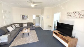 A living room with a grey sectional sofa, a coffee table, a flat-screen TV on a wooden stand, and a patterned rug. - Susie's Beach House - South West Rocks (SOUTH WEST ROCKS)