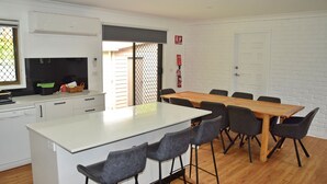 Una cocina moderna con armarios blancos, una isla central con taburetes y una mesa de comedor con sillas.