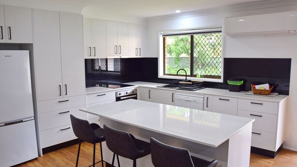 Cocina moderna con armarios blancos, una isla central con taburetes de bar, encimera negra y ventana con vistas a la vegetación.
