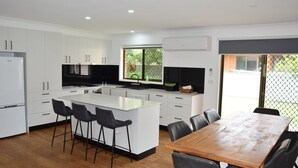 Una cocina moderna con armarios blancos, una isla central con taburetes de bar, una mesa de comedor de madera y un ventanal con vistas a zonas verdes.