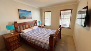 A bedroom with a wooden bed, two bedside tables with lamps, a painting on the wall, and two windows with blinds. - Dunbar Court Unit 7 - South West Rocks (SOUTH WEST ROCKS)