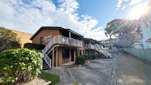 A two-story building with a sign reading 'Dunbar Court.' There is a staircase leading to the upper floor, and the building is surrounded by a low fence and greenery. - Dunbar Court Unit 7 - South West Rocks (SOUTH WEST ROCKS)