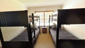 Een kamer met stapelbedden, een klein raam en een vloerkleed.