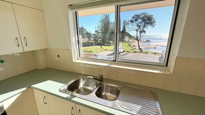 Una cocina con un lavaplatos doble de acero inoxidable, una ventana con vista a un parque y una masa de agua, y armarios de color claro.