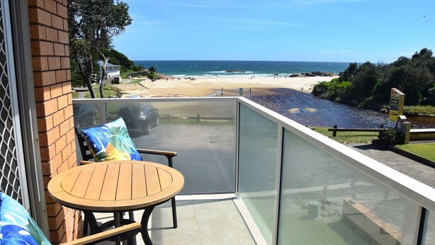 Un balcón con mesa y sillas de madera, con vista a una playa y un río.