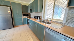 A kitchen with teal cabinets, a stainless steel refrigerator, a microwave, a toaster, and a dishwasher. - Village Centre 3 - South West Rocks (SOUTH WEST ROCKS)