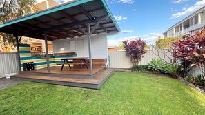 Ein Garten mit überdachter Terrasse, einem Holztisch und einem Rasen.