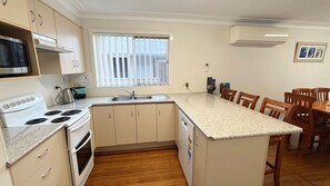 A compact kitchen with a stove, microwave, sink, and a small island with chairs.