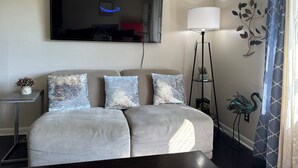Een moderne woonkamer met een bank, een vloerlamp en een flatscreen televisie aan de muur.