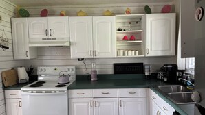 Een keuken met witte kasten, een fornuis, een spoelbak en een koffiezetapparaat.