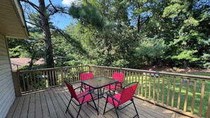 Een houten terras met een tafel en rode stoelen, omgeven door bomen en een hek.