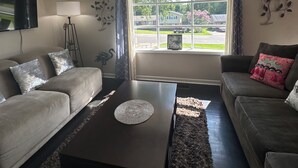 Een woonkamer met een bank, een salontafel, een lamp en een raam met uitzicht op het buitengebied.