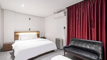 Una habitación de hotel con cama, mesita de noche, sofá de cuero negro, cortina roja y radiador.