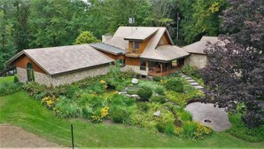 Ein Haus mit Steinaußenwand, einer Holzdielen-Terrasse und einem Garten mit verschiedenen Pflanzen und Blumen.