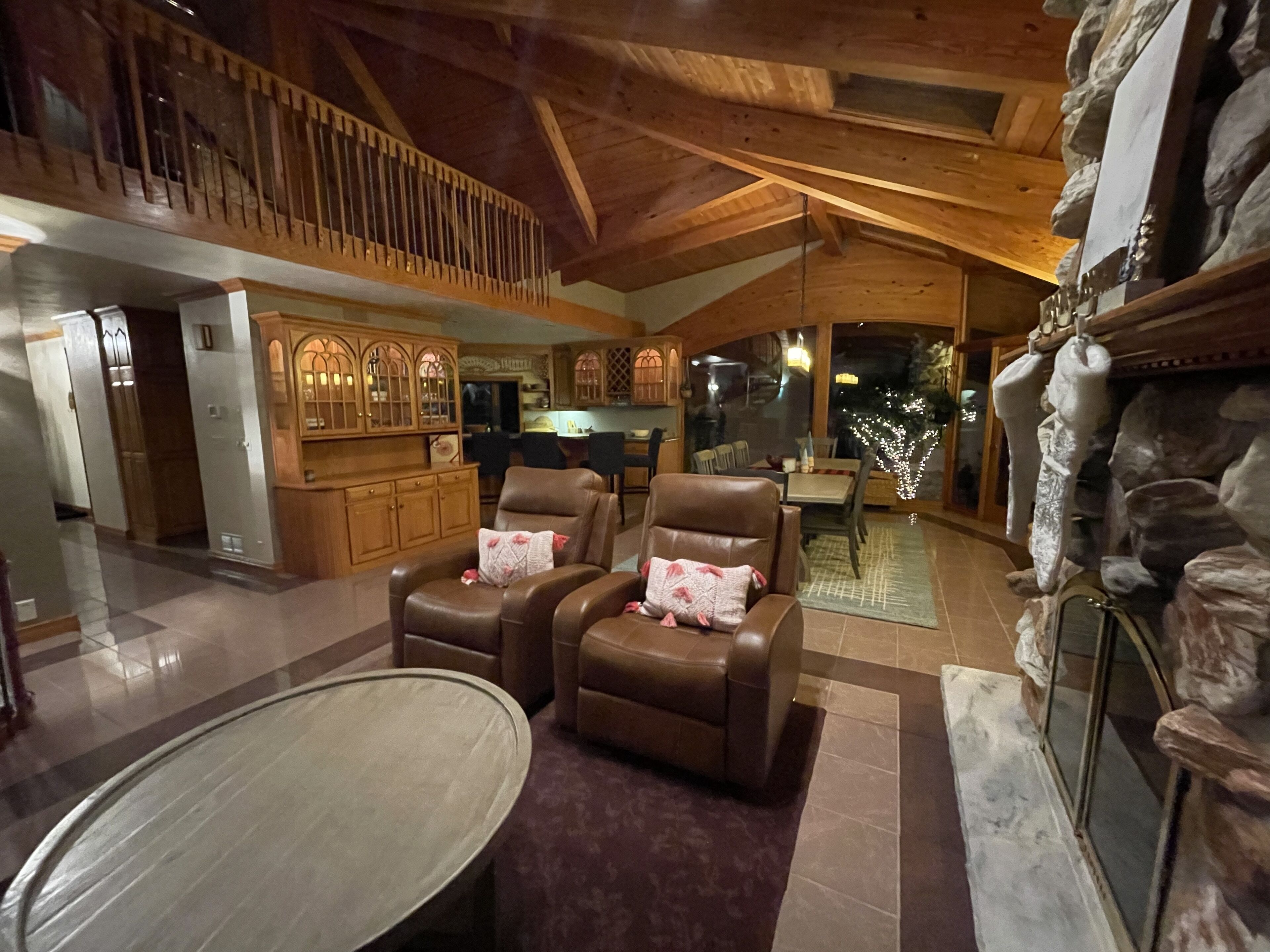 Un vaste espace de vie doté d’un plafond haut et de poutres en bois, comprenant des fauteuils en cuir, une table à manger et une cheminée en pierre.