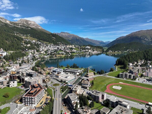 A town with a lake, surrounded by mountains, featuring modern buildings, a sports field, and a road network.