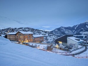 Een hotel met meerdere verdiepingen, een skilift en besneeuwde bergen op de achtergrond.
