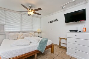 A bedroom with a bed, a ceiling fan, a TV, a dresser, and a wall-mounted shelf.