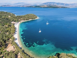 Vue aérienne d’une zone côtière avec des eaux cristallines, une plage et deux voiliers.