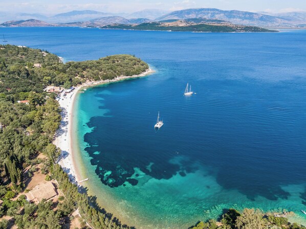 An aerial view of a coastal area with clear waters, a beach, and two sailboats.