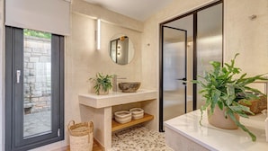Un baño moderno con pared de piedra, un espejo redondo, un lavamanos y una planta en maceta.