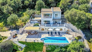 Una casa de dos pisos con piscina, muros de piedra y mobiliario exterior.