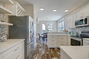 A kitchen with white cabinets, a stainless steel refrigerator, a microwave, and a tiled backsplash.