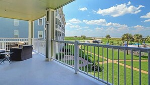 A balcony with outdoor furniture, a view of a golf course, and a clear sky.
