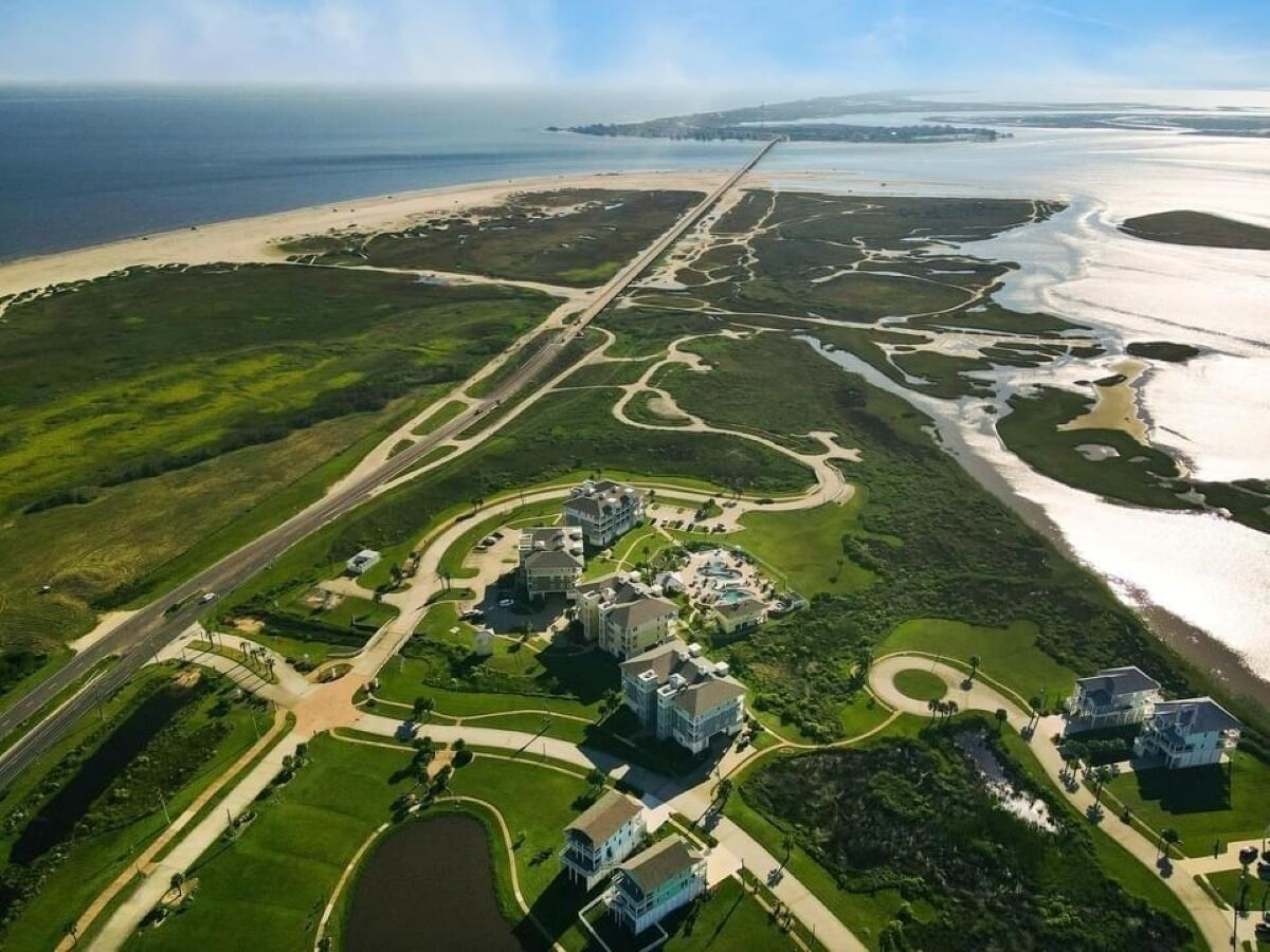 An aerial view of a coastal resort with multiple buildings, roads, and a beach.
