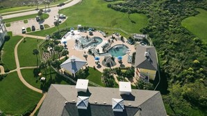 An aerial view of a golf course with a swimming pool area, surrounded by lush greenery and a body of water.