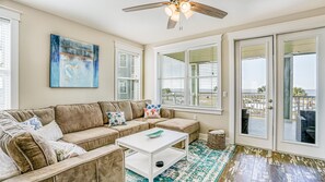 A living room with a beige sectional sofa, a white coffee table, and a large window with blinds.